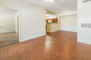 an empty living room with a kitchen in the background